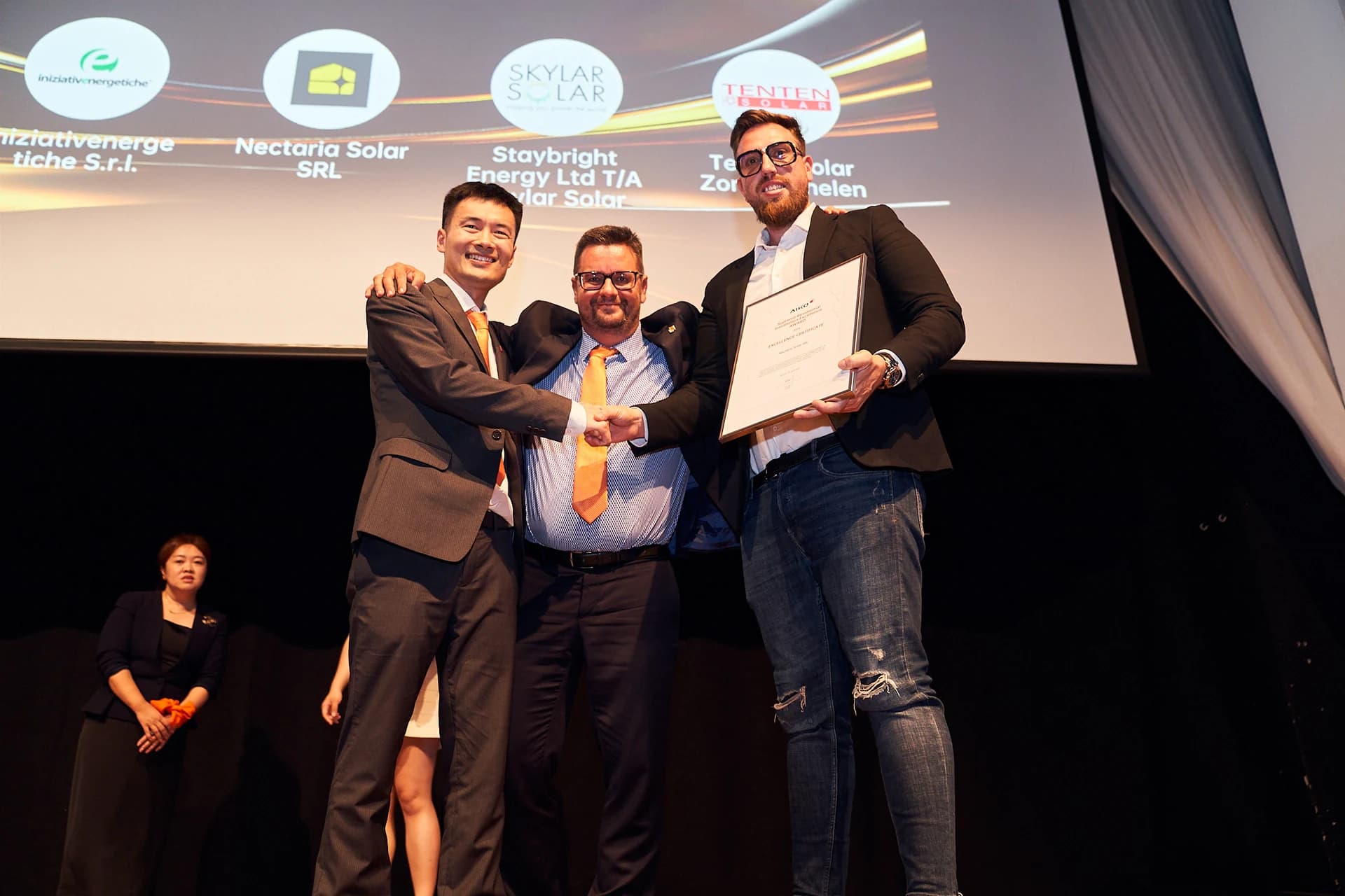 Nectaria Solar representatives at an AIKO event, holding a residential installation recognition certificate, with the company name on screen
